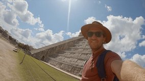 Young man taking selfie portrait at Chichen Itza Mayan temple in Mexico having fun exploring while on vacations. Traveler capturing selfie video in front of mayan pyramid - slow motion 