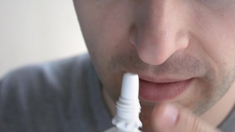 Man gets flu, guy blows his nose and uses nasal spray, man's face, close-up