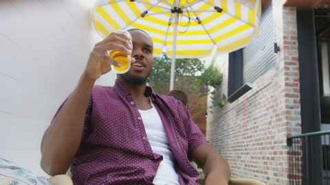 Young attractive man sitting at restaurant talking to friend having a beer on a patio with other patrons in the background. Medium close on 4k RED camera.