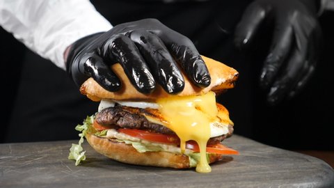 Male chef hand pressing juicy burger dripping sauce and yolk in slow motion. American Burger with Egg and fresh vegetables, served in restaurant, close-up view, Full hd