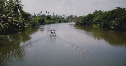 Camera follows little white boat sailing along beautiful calm river in the middle of the rainforest jungle wilderness. Stock Video