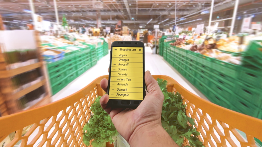 Supermarket store cart timelapse holding smartphone with shopping grocery list on the screen 4k Royalty-Free Stock Footage #1045990399