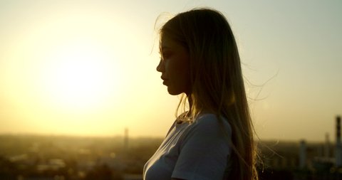 Close up poerrait of young caucasian girl standing on rooftop during beautiful sunset, looking far away - freedom, youth concept 4k footage