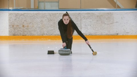 Curling training - a young woman with long hair pushes off from the stand - leading the stone biter
