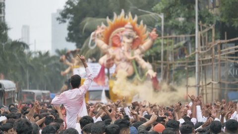 A giant Ganapathi idol driven in the street for immersion. Slow motion shot of People are celebrating. throwing colors and dancing in front of the grand Ganapati idol, Mumbai, India (August 2019)