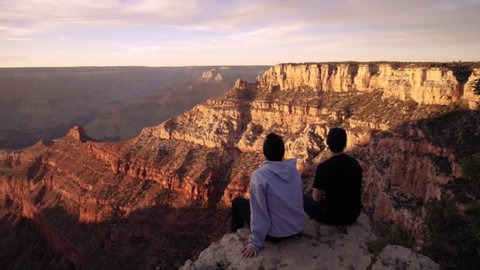 Young couple sitting on the south rim of Grand Canyon at sunset.