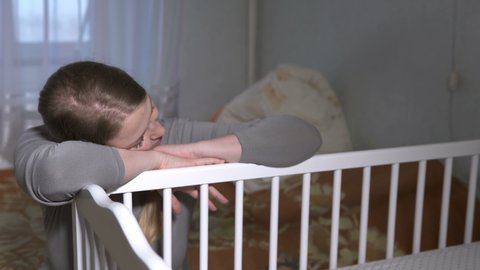 Tired woman fell asleep near the crib of a newborn daughter. The concept of motherhood.