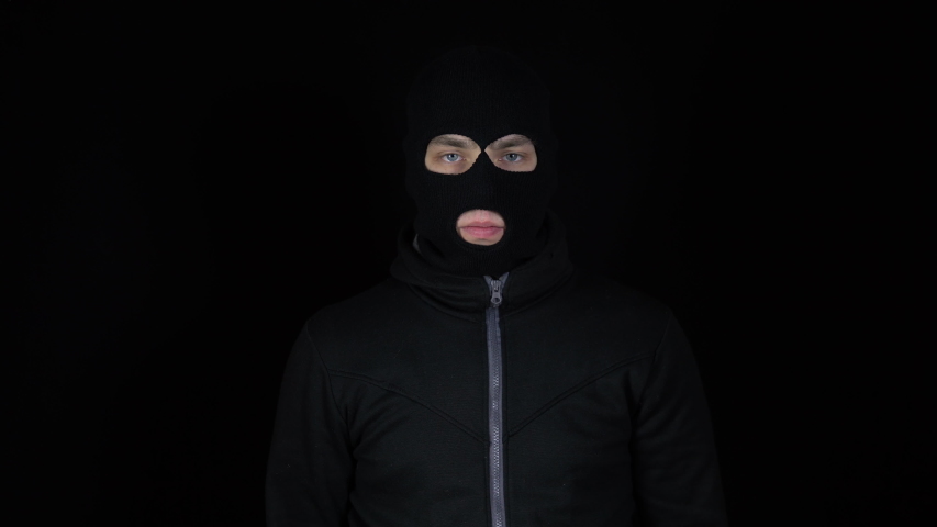 A man in a balaclava mask stands with a pepper spray. Pepper spray self defense weapon. On a black background.