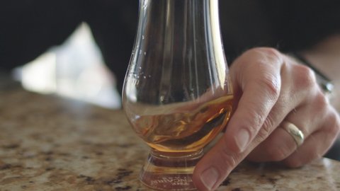 Man swirling whiskey in a glencairn glass on a multi-colored counter top.