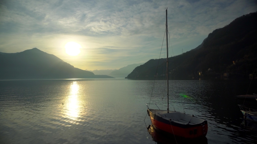 Sailing yacht moored off the coast on Lake Como in Italy before sunset over the mountain horizon of alpine peaks. Cinematic frame. Romantic atmosphere. Calm and pacifying scene. Sailboat Royalty-Free Stock Footage #1046020255