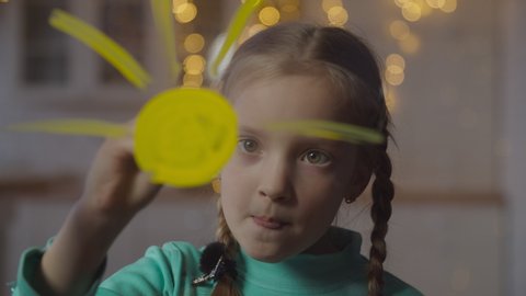Lovely elementary age girl with pigtails painting sun on window glass with paintbrush and yellow paint at home. Positive little artist drawing on window, expressing her imagination and creativity.