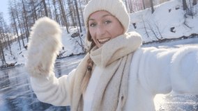 Young woman iceskating on frozen lake takes a selfie. Female outdoors enjoying winter vacation activity taking video selfie