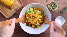 Hands mix summer vegetable salad with spinach, cherry tomatoes, avocado, grilled corn and pumpkin seeds. Healthy eating concept, top view.