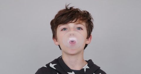 Happy boy chewing gum and learning to inflate bubbles and bursting it joyfully smiling looking at camera slow motion on white background. Child. Childhood. Emotions of people. Life style