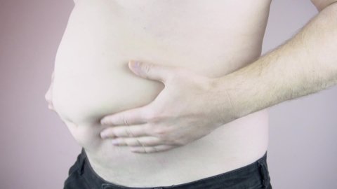 A man shows a big belly. Obesity. Overeating problem. Close-up. Slow motion.