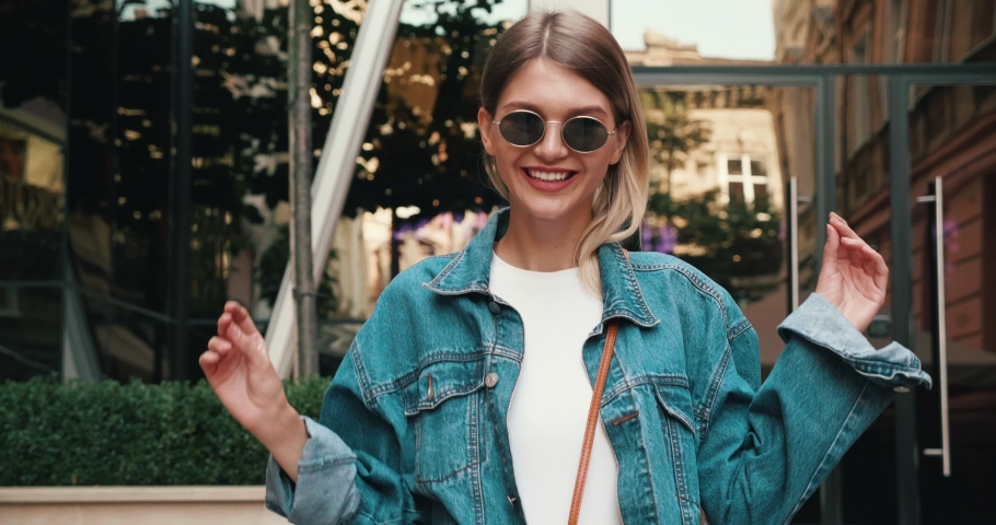Portrait of Young Funny girl walking in the Town and enjoying her Life, Looking Smiling. Satisfied and Pleasant Woman Wearing Oversize Jeans Jacket. Having trendy round Sunglasses. Royalty-Free Stock Footage #1046052805