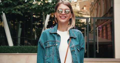 Portrait of Young Funny girl walking in the Town and enjoying her Life, Looking Smiling. Satisfied and Pleasant Woman Wearing Oversize Jeans Jacket. Having trendy round Sunglasses.