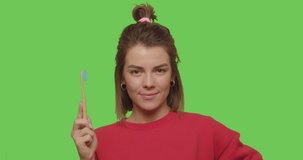 Attractive good looking woman smiling and showing her teeth, demonstrating simple bamboo eco-friendly toothbrush made of wood on chroma key. Zero waste concept. 4k raw video footage slow motion