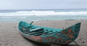 Peaceful boat on the beach, white waves crashing on the shore nearby, windy sea, 4K video. A traditional wooden boat with many patterns painted on the hull. Footage was recorded on Ly Son island