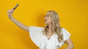 Beautiful blond woman making selfie on smartphone isolated over yellow background