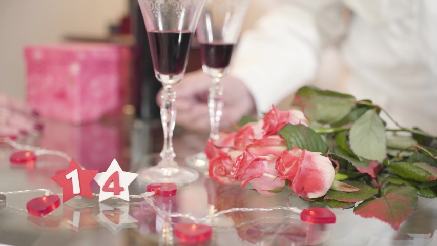 Close-up of bouquet of roses and wineglasses standing on glass table. Mature male hand taking senior wife
