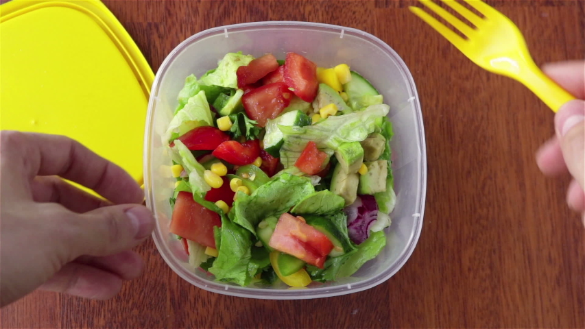 fresh salad with  cucumber  tomaotes avocado corn  parsley in  plastic food container