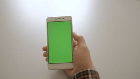 A man connects a headset to a smartphone to listen to music and watch movies. Male using smartphone with green screen while sitting on in room. 