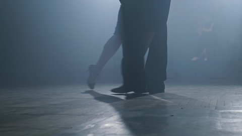 Legs of couple dancing tango in smoky studio in slow motion. Young couple dance tango in dark room with spotlights. Close-up shot in 4K, UHD