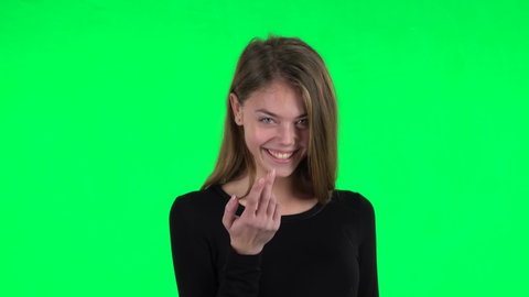 Young woman coquettishly smiling, waving hand and showing gesture come here. Green screen