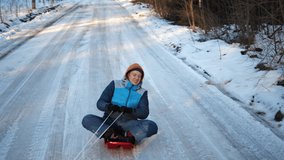Happy funny young man is sledding on snowy road in winter forest mountains at daytime. Winter activities. Fun and leisure concept.