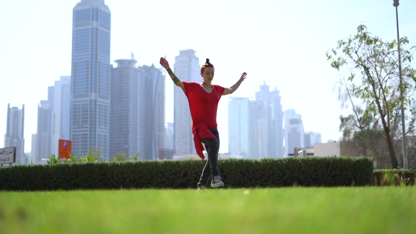 Young woman jumping high performing acrobatic on the green grass outdoors in Dubai city 