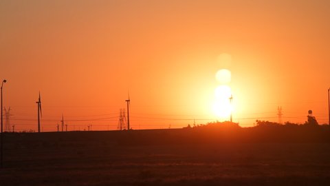 Snyder, USA view of wind turbine farm and power lines in Texas countryside industrial town and horizon with timelapse of colorful red sunrise