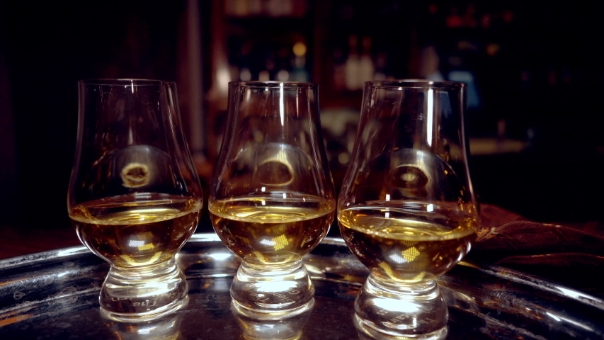 Three tasting glasses for whiskey  (glencairn) with a drink on a tray, with a fixed camera. Movement around the bar.