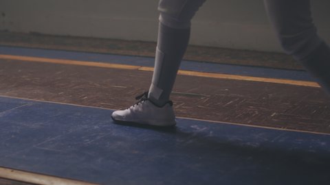 Close-up pan of a female fencer training on a strip in a dark and dusty fencing gym