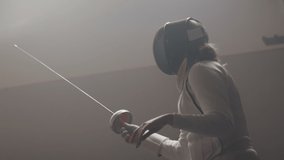 A female fencer raises her epee in a dark and dusty fencing gym in slow motion - Powered by Shutterstock - Get 15% off with code: PIKWIZARD15
