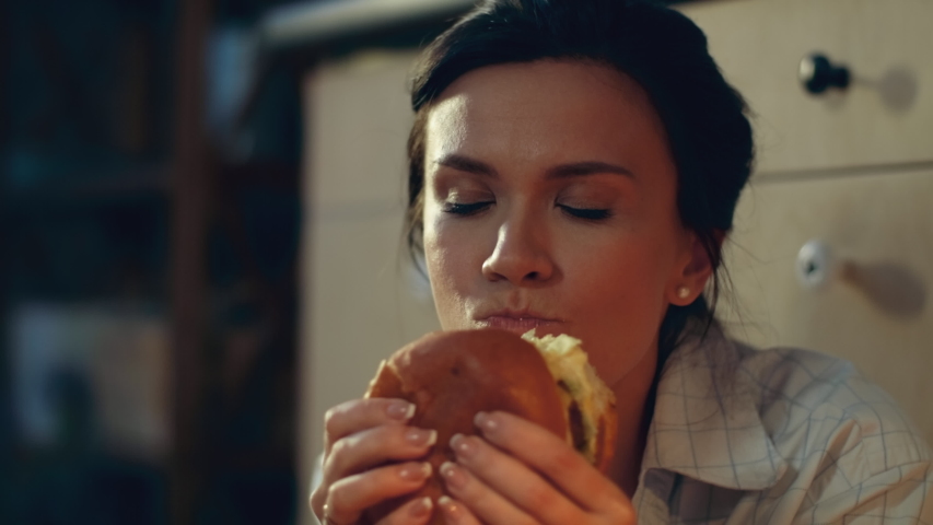 Closeup hungry girl eating big burger on kitchen floor. Portrait of young woman drinking red wine evening at home floor. Joyful woman enjoying fast food dinner and wine at home in slow motion. Royalty-Free Stock Footage #1046119030