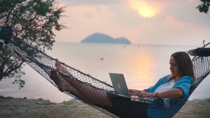 Young woman freelancer lying in a hammock with a laptop on the tropical beach at the sunset time. | Shutterstock HD Video #1046119177