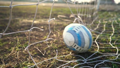 Kyiv, UKRAINE - January 2, 2020: Close-up of a torn soccer net. Soccer ball through the net. Old gate soccer field. Street sport. Child Game. The sun shines through the grid. The crisis. Football.