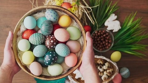 Hands holding basket full of colorful Easter eggs in front of decoration on wooden table. Easter holiday decorations, Easter concept background.
