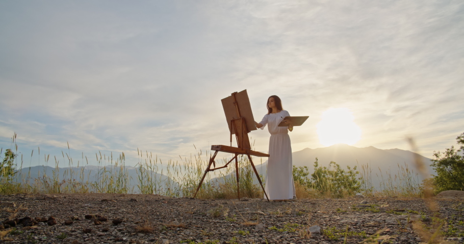 Multiethnic girl enjoying her hobby in mountains, creating an art piece on easel inspired by view - recreational pursuit, inspirational landscape concept 4k footage