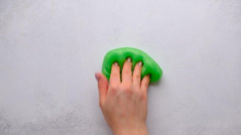 Woman hands playing with green slime on white background. Trendy liquid toy. Top view. 4k footage.