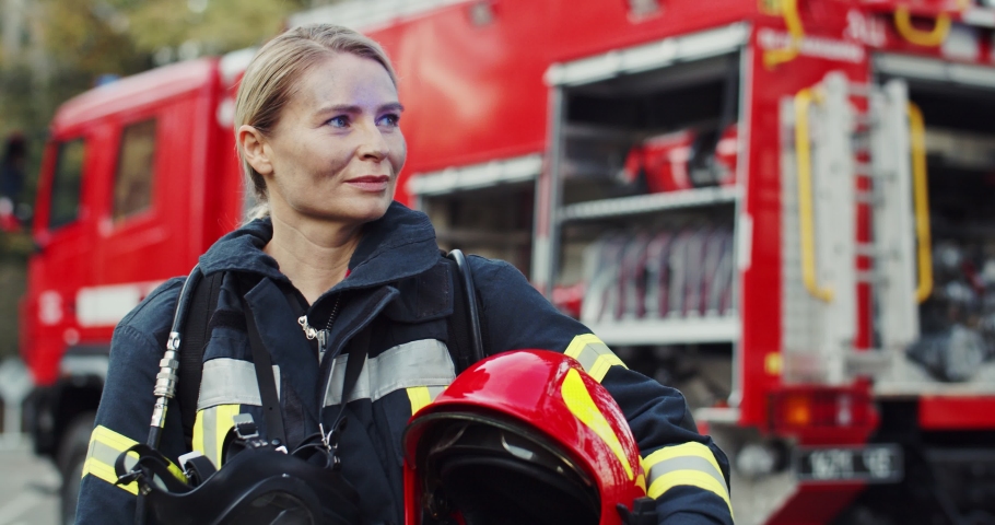 Portrait shot of the happy Caucasian young woman firefighter with the helmet in hand smiling to the camera after fire at the red truck. Outside. Royalty-Free Stock Footage #1046145193