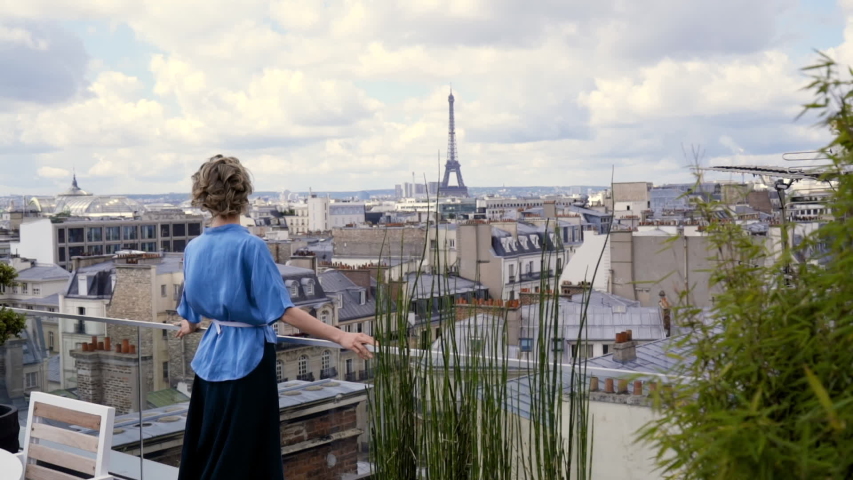 Back view of a woman in blue shirt stands on the roof and looks at the eiffel tower, Paris
