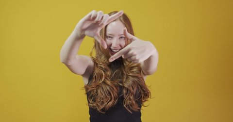 Redhead caucasian woman over yellow isolated background smiling making frame with hands and fingers with happy face. Creativity and photography concept. Film-maker or photographer. Lens vision idea.
