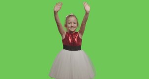 Friendly girl waving hand smiling greeting welcoming over green screen background. Cheerful pretty female kid wearing ball dress on chroma key. 4k raw video footage slow motion