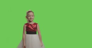 Kid wearing ball dress like princess pointing to side and upwards showing object in copy space over green screen background. Girl having fun on Chroma Key. 4k raw video footage slow motion 60 fps