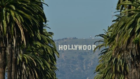 Los Angeles, California / USA - February 8th 2020: Zoom in to a famous Hollywood sign seen from far away through palm trees. Heat and air diffraction seen as waves. 