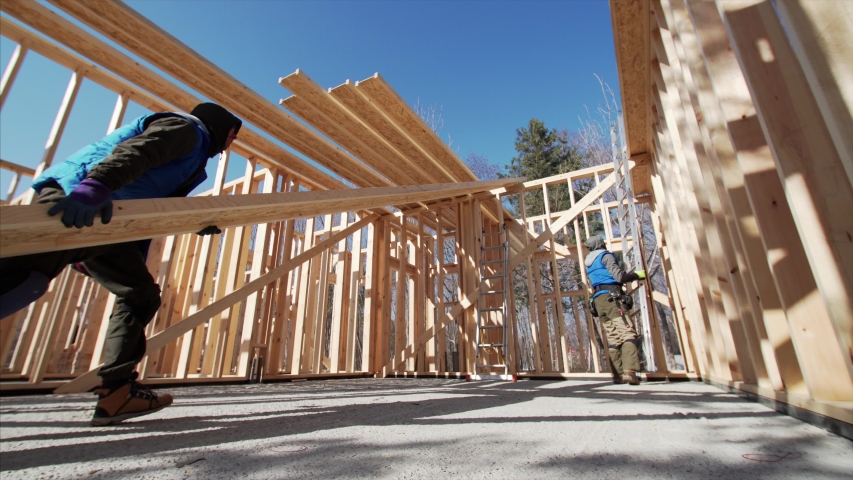 Sliding view of two workers carrying long heavy beam. Frame house site building. Sunny day | Shutterstock HD Video #1046158732