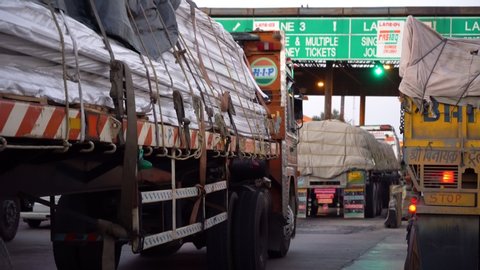 Delhi, India - circa 2019 : Trucks loaded with cargo crossing an NHAI toll booth with green boards covered with Fastag no cash stickers post the mandatory implementation. The trucks and cars can cross