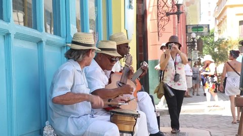Havana / Cuba - July 2,2017: A group of street musicians in Havana, Cuba energetically perform their music as a tourist takes pictures of them in the background.